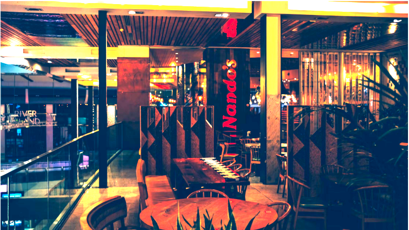 A picture of the inside of a Nando's restaurant. There are tables and chairs, and a bar. The restaurant lighting gives an ambient atmosphere.